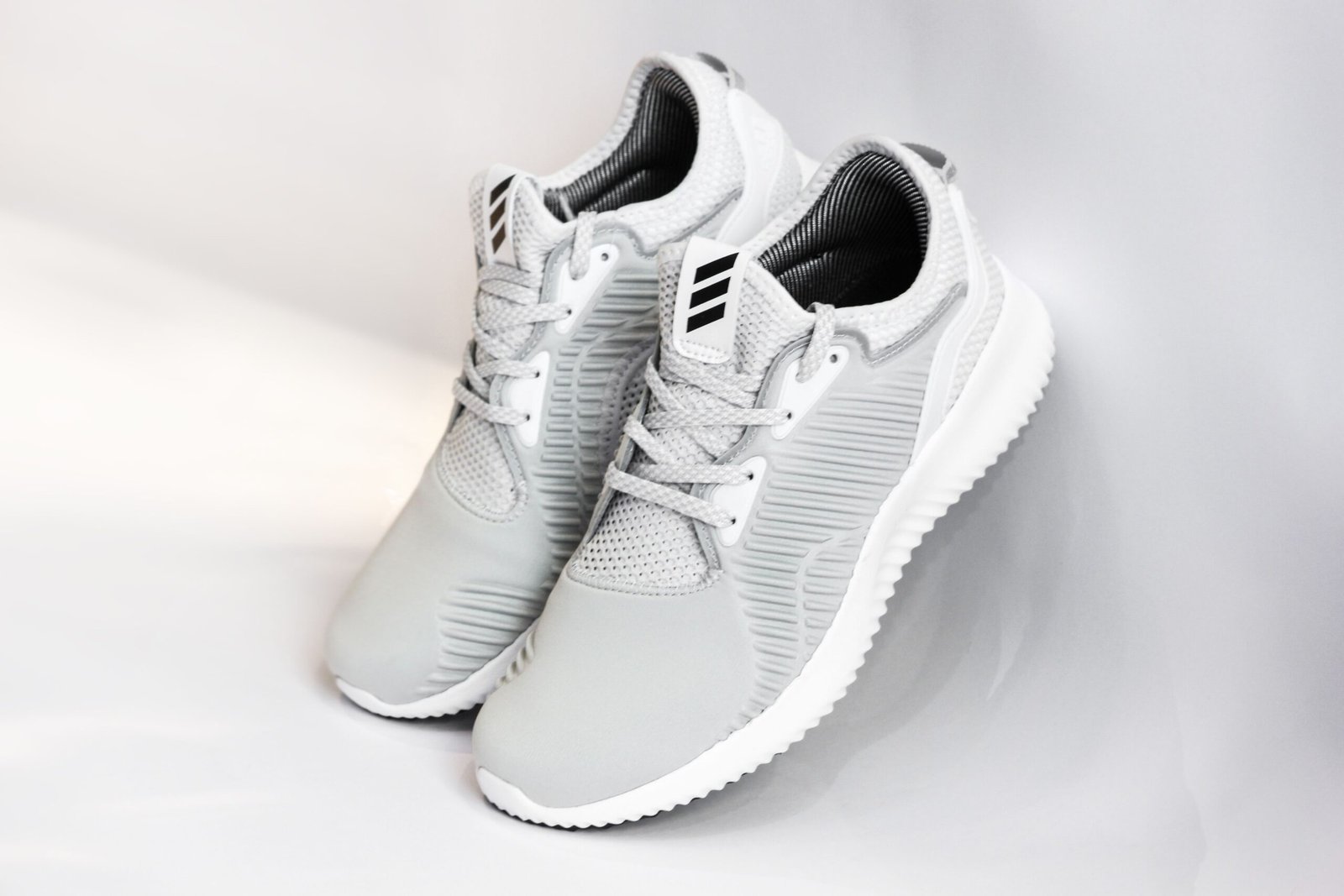 Pair of sports shoes with gray dense texture of surface and rubber inserts from sided and laces and white soles placed with heels up leaning on glance gray background