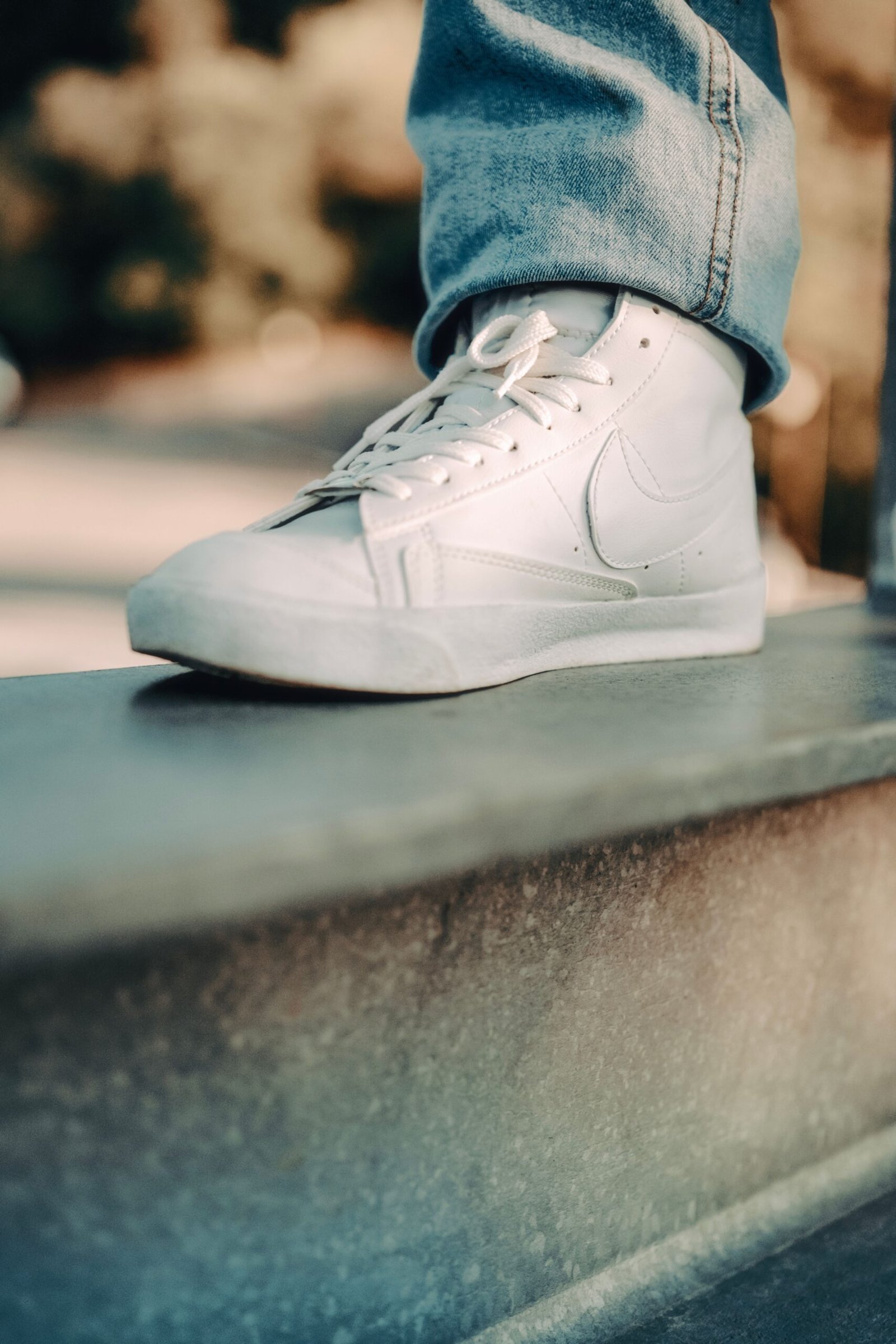 Detailed close-up of a white sneaker on an urban ledge, emphasizing modern footwear style.