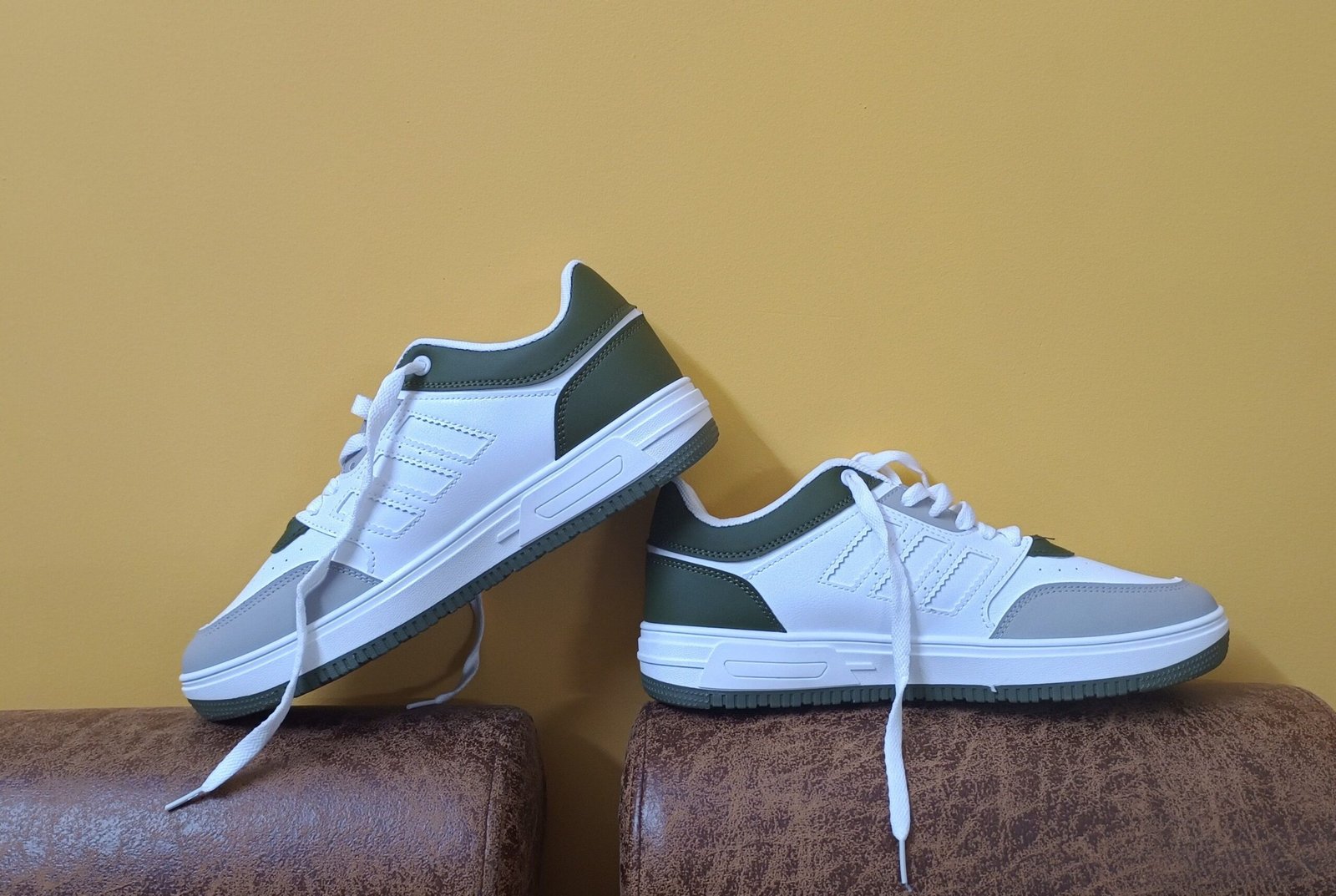 White and green casual shoes elegantly displayed against a yellow backdrop, perfect for fashion concepts.